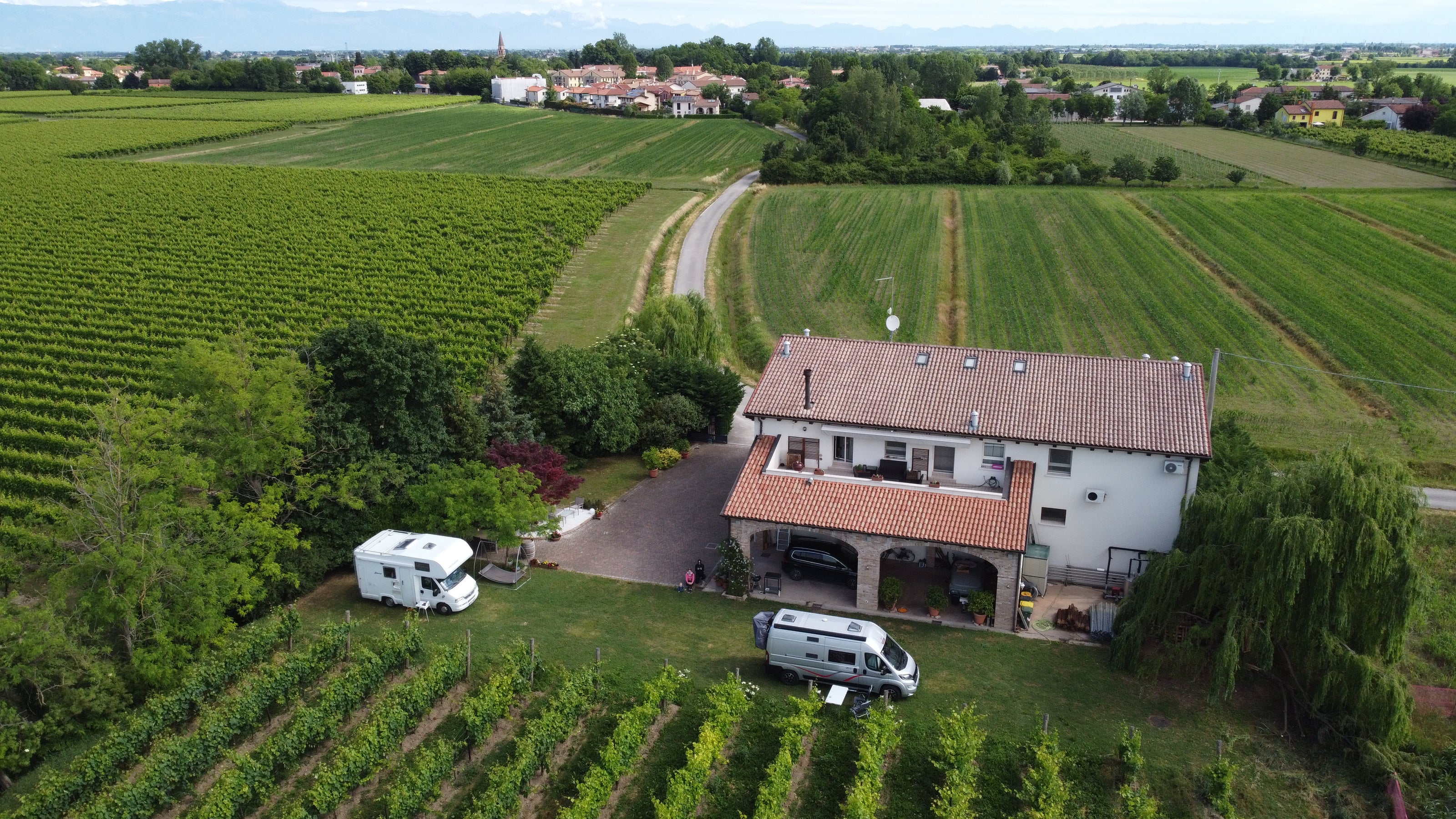 Das Weingut Sfriso von einer Drohne aus gesehen, die die vor dem Weinberg geparkten Wohnmobile und das von grünen Feldern umgebene Weingut zeigt